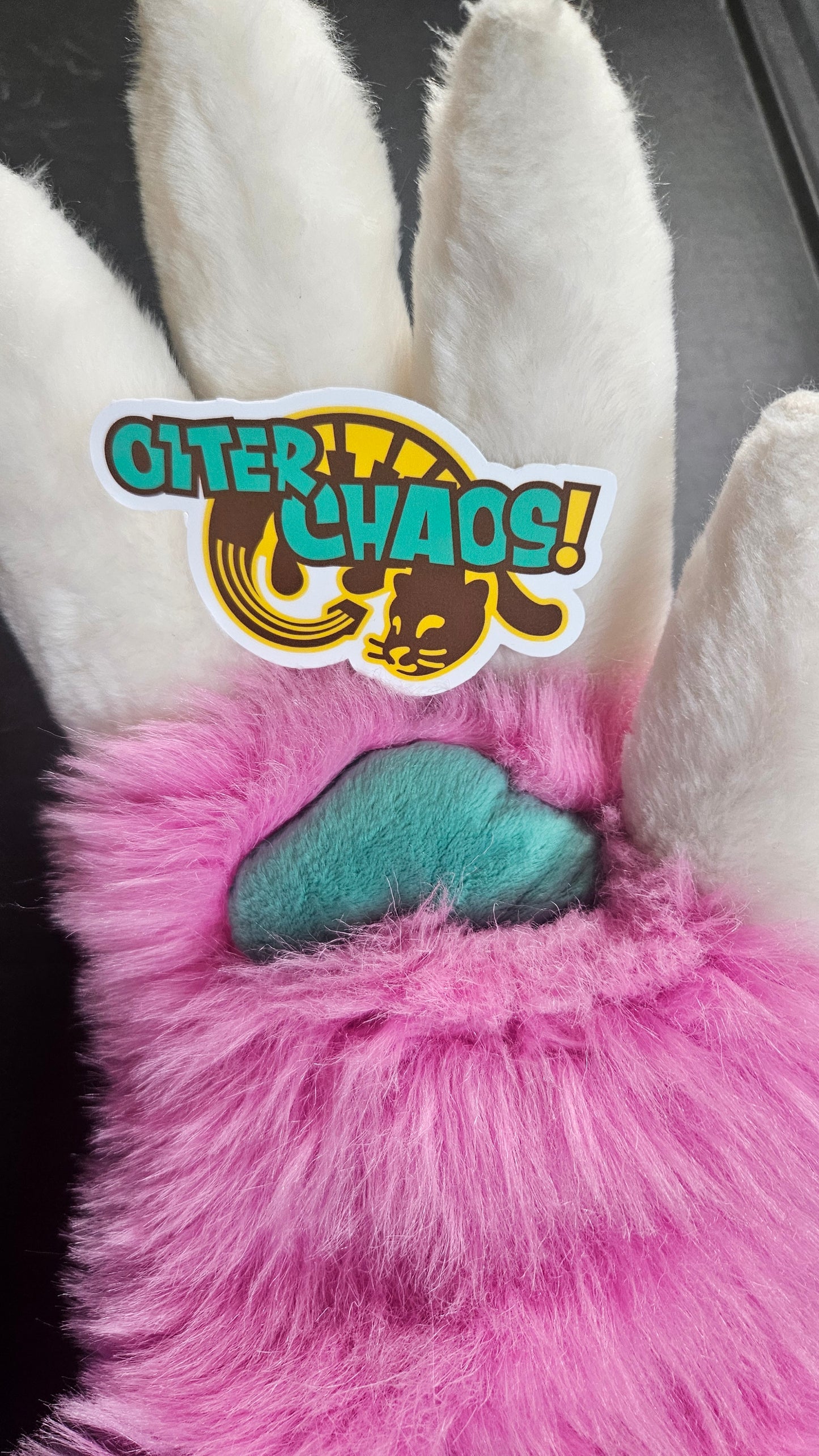 Rhubarb's fursuit paw holding the Otter Chaos! sticker to show it off